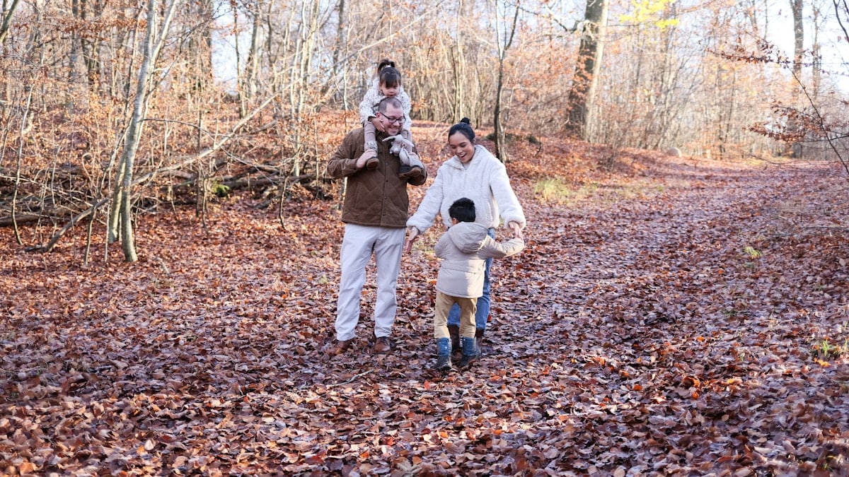 Family walking on a leaf-covered path in autumn woods.